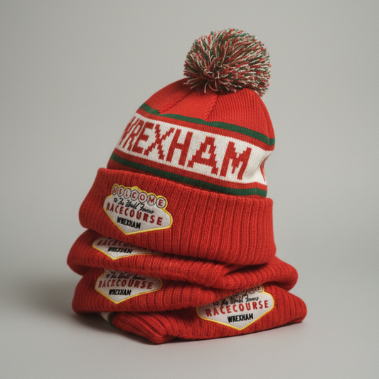 Stack of red Wrexham USA knitted beanies with pom-poms on a gray background